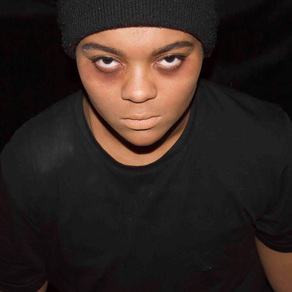 a black man in a black beanie and a dusty black t-shirt. he has dark circles under his eyes. he looks like death.