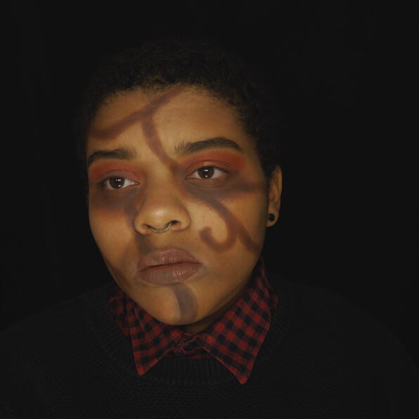 a black man with short hair, round black earrings, and a septum ring. he has brown twisting vines on his face. he is afraid.