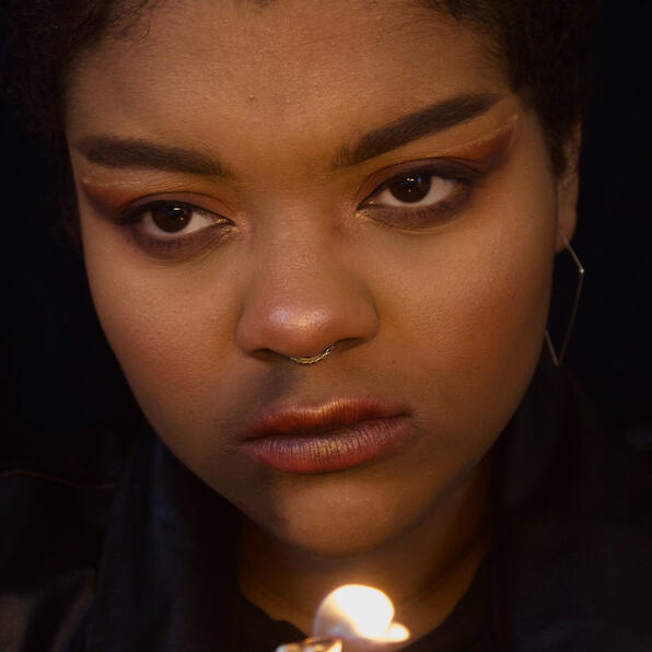 a black man with a septum piercing, smokey eyes, and burning lips. smoke pours from his nose. he holds a lit lighter.