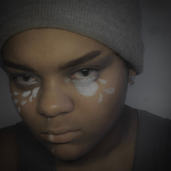 a black man in grey clothing. mist pours in tears from his nose and eyes. his eyes are clouded, staring at you.