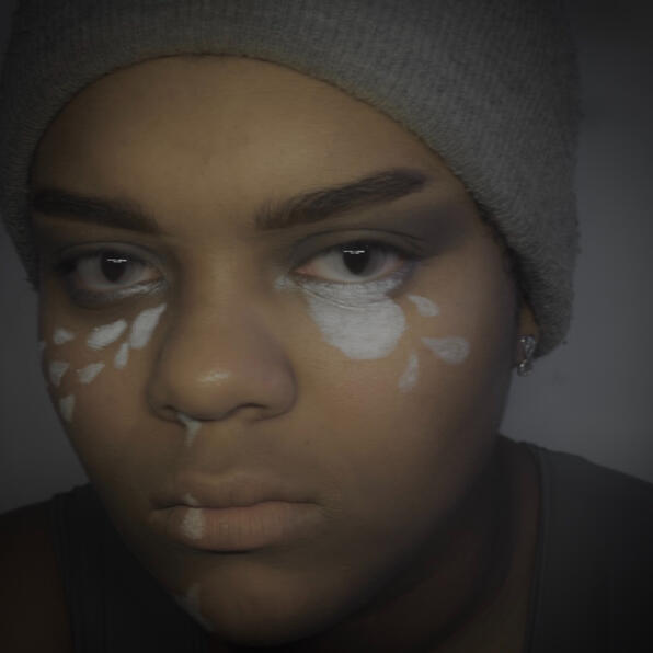 a black man in grey clothing. mist pours in tears from his nose and eyes. his eyes are clouded, not quite focusing on you.