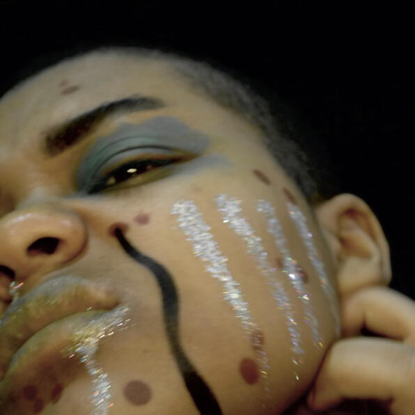 a black man, pock-marked, with green mold on his eyes and black and silver fluid oozing. he scratches.